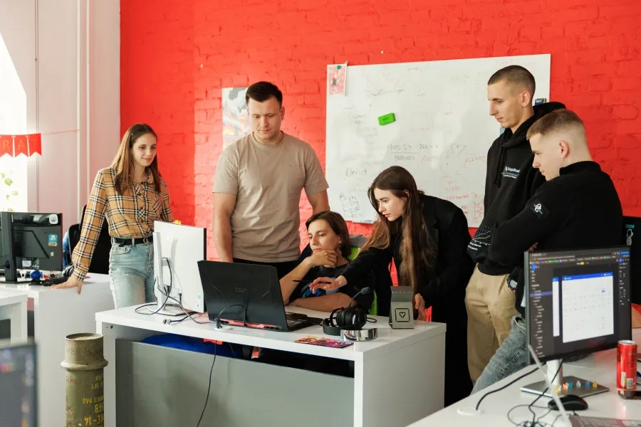 A group of six people gathered around a desk with computers, collaborating on a project.